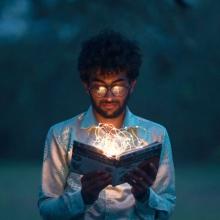 Man looking at an open book with glowing fiberoptic lights