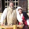 photo of John and Jan Haigis standing outside by a split-rail fence on a sunny day, wearing pioneer costumes